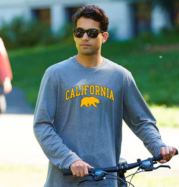 A boy wearing grey california t-shirt holding a bicycle
